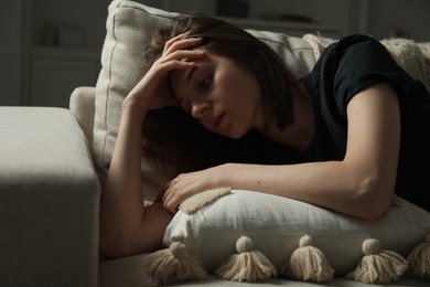 Photo of Sad young woman lying on sofa at home