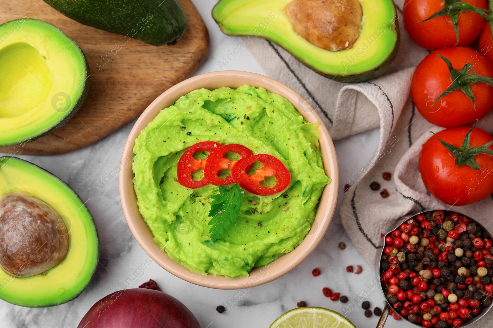 Photo of Bowl of delicious guacamole and ingredients on white marble table, flat lay