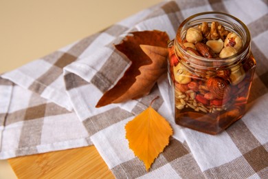 Different nuts with honey in jar and dry leaves on wooden table. Space for text