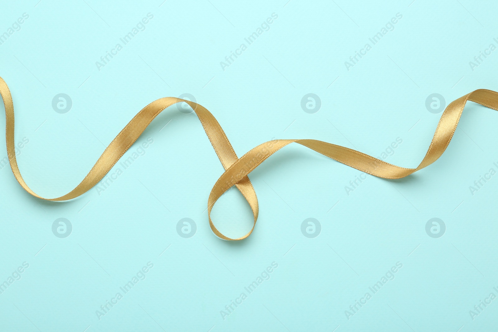 Photo of Beautiful golden ribbon on light blue background, top view