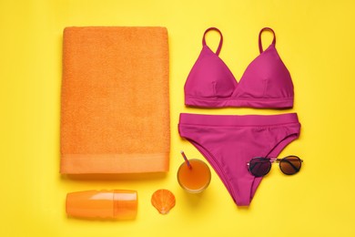 Beach towel, swimsuit, sunglasses and sun protection product on yellow background, flat lay