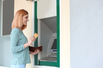 Photo of Beautiful woman with credit card near cash machine outdoors, space for text