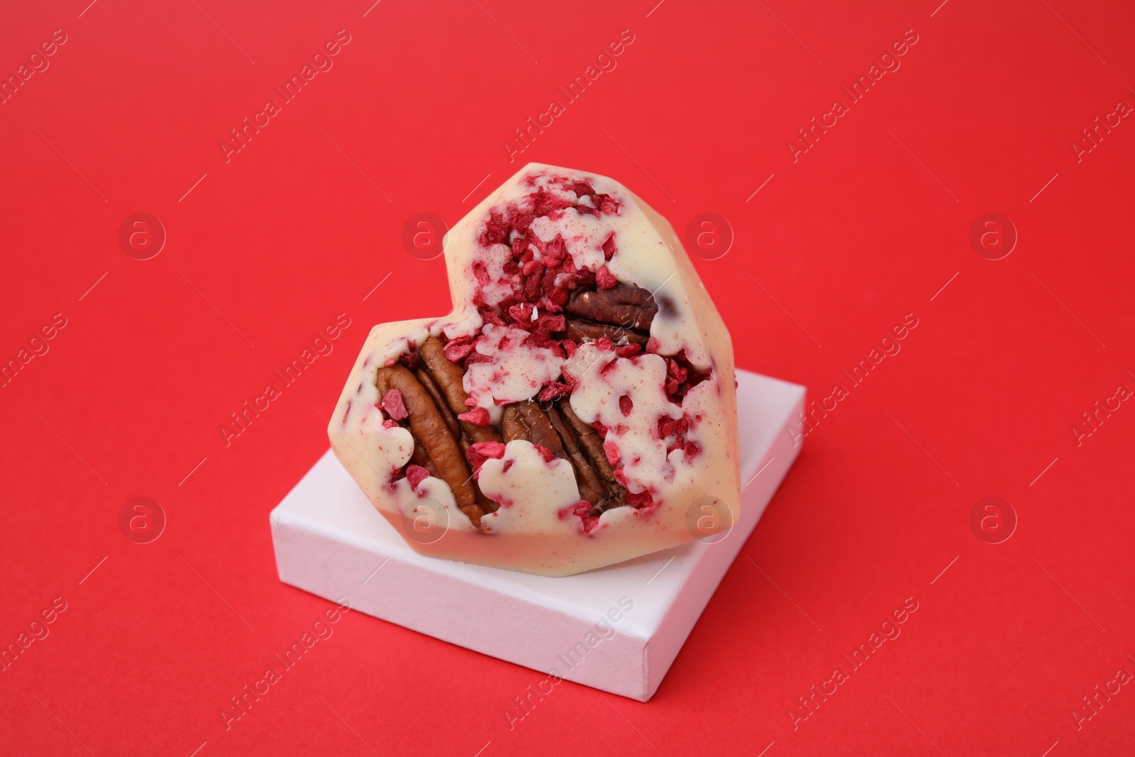 Photo of Tasty chocolate heart shaped candy with nuts on red background