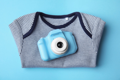 Photo of Toy camera and children's shirt on light blue background, top view. Future photographer