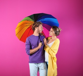 Couple with rainbow umbrella on color background