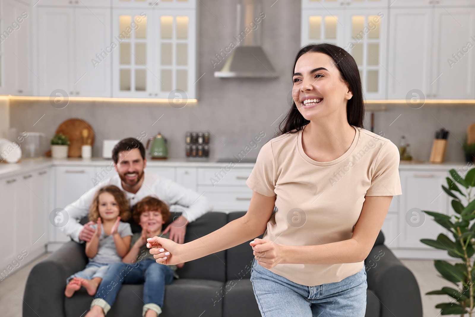 Photo of Happy family having fun at home. Mother dancing while her relatives resting on sofa