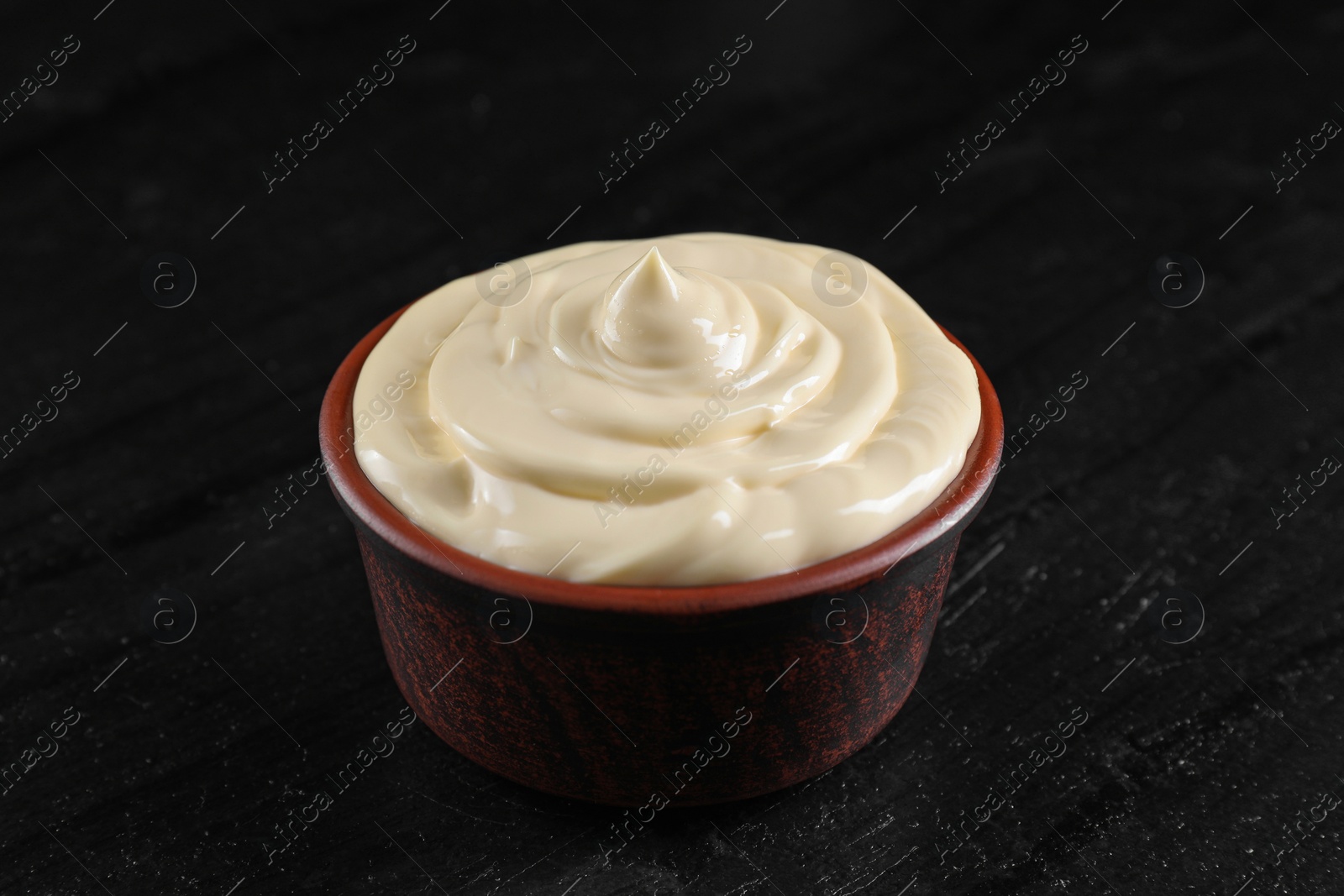 Photo of Fresh mayonnaise sauce in bowl on black table, closeup