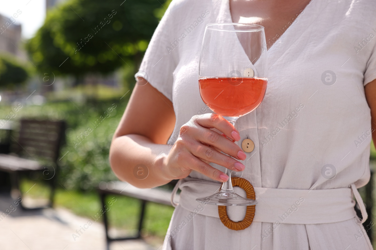 Photo of Woman holding glass of rose wine outdoors, closeup. Space for text