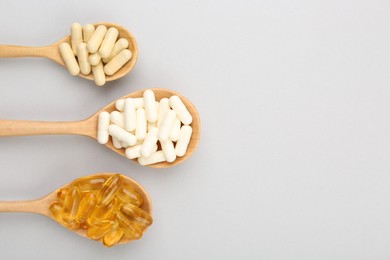 Wooden spoons with different vitamin capsules on light grey background, flat lay