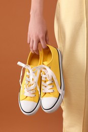 Photo of Woman with yellow classic old school sneakers on brown background, closeup