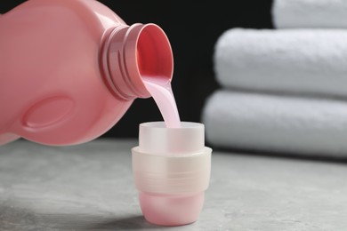 Photo of Pouring laundry detergent from bottle into cap on light grey marble table, closeup