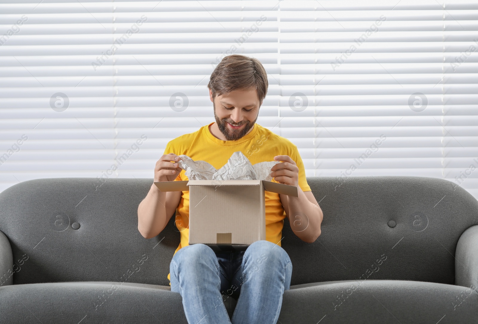 Photo of Happy man opening parcel at home. Internet shopping