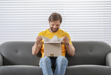 Happy man opening parcel at home. Internet shopping