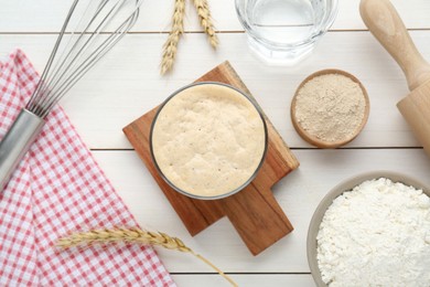Leaven, flour, water, rolling pin, whisk and ears of wheat on white wooden table, flat lay