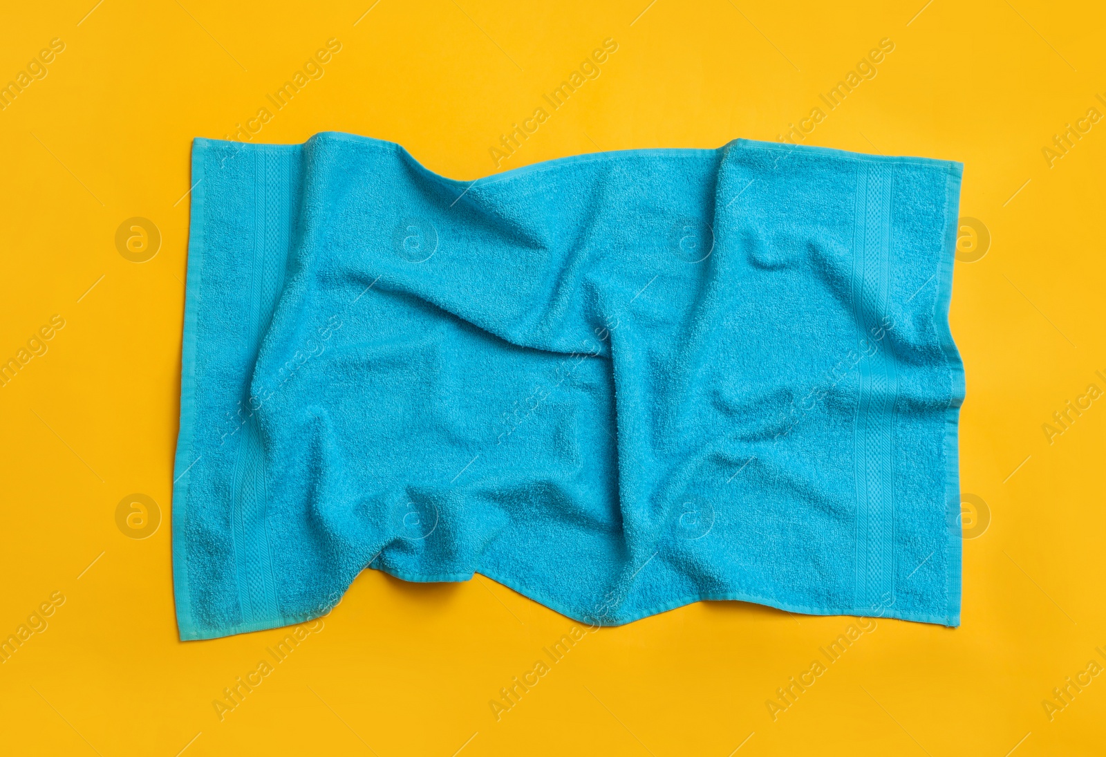 Photo of Crumpled light blue beach towel on yellow background, top view