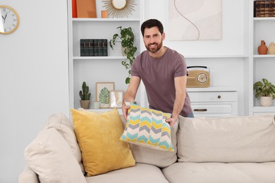 Photo of Spring cleaning. Man putting pillow on sofa in living room