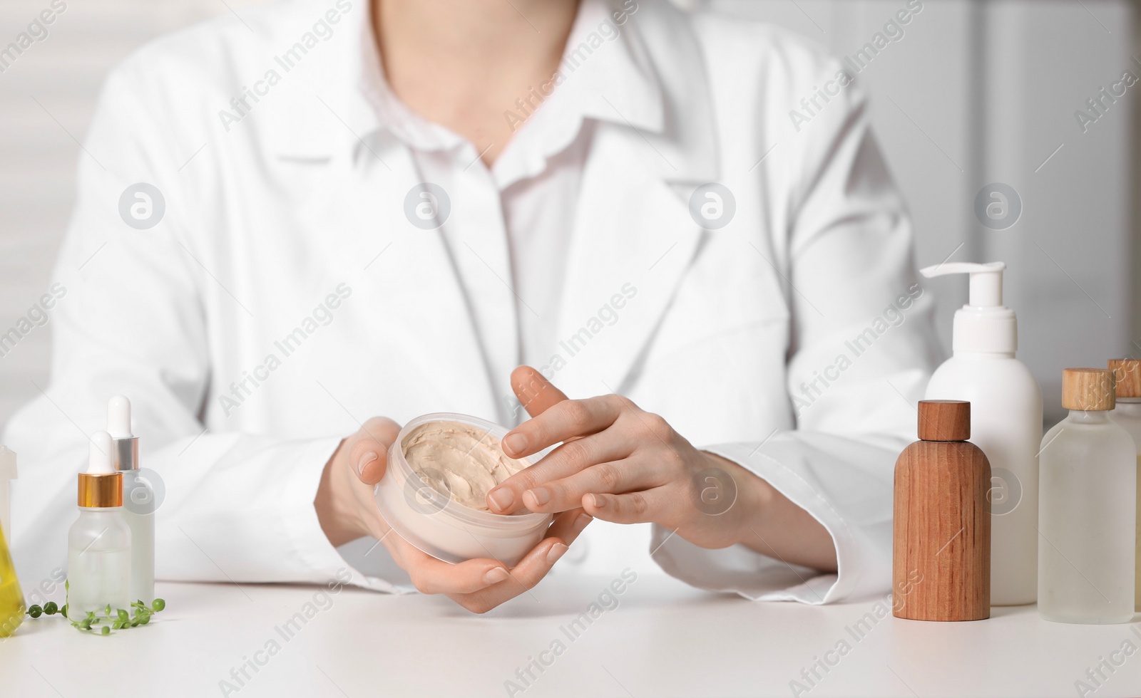 Photo of Dermatologist with jar testing cosmetic product at white table indoors, selective focus