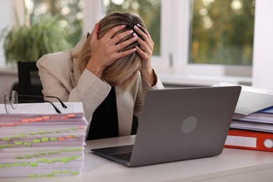 Photo of Overwhelmed woman sitting at table with stacks of documents and folders in office