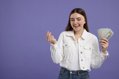 Happy woman with dollar banknotes showing money gesture on purple background, space for text