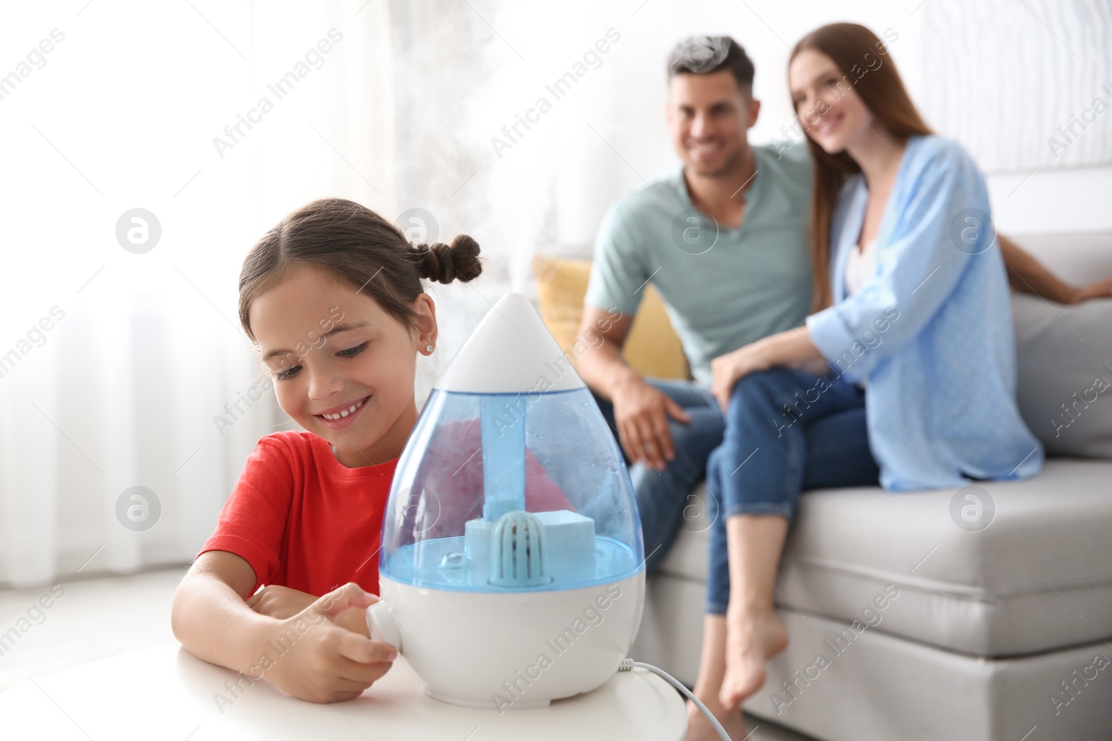 Photo of Little girl using modern air humidifier near her parents at home