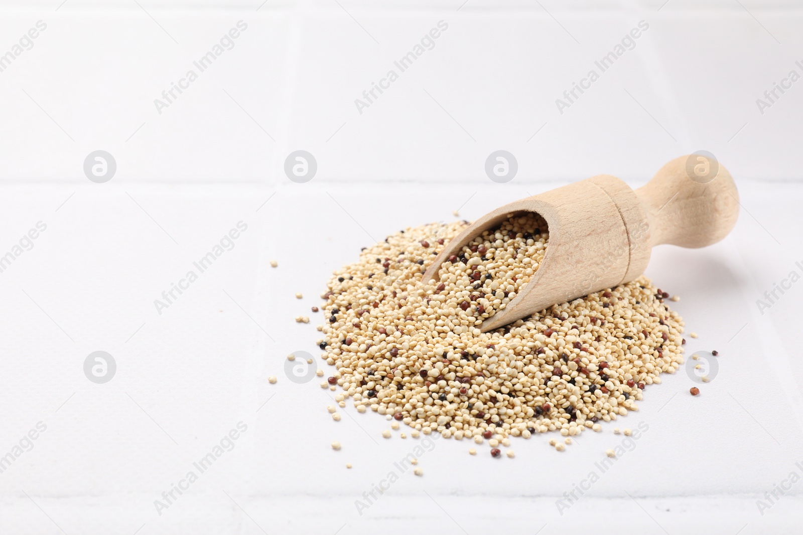 Photo of Scoop with raw quinoa seeds on white tiled table. Space for text