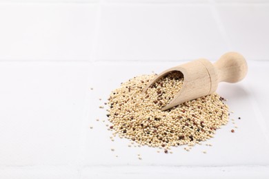 Photo of Scoop with raw quinoa seeds on white tiled table. Space for text