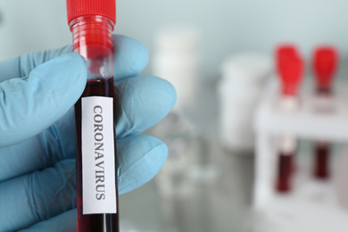 Doctor holding test tube with blood sample and label CORONAVIRUS in laboratory, closeup of hand