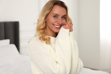 Happy woman in stylish warm sweater on bed at home