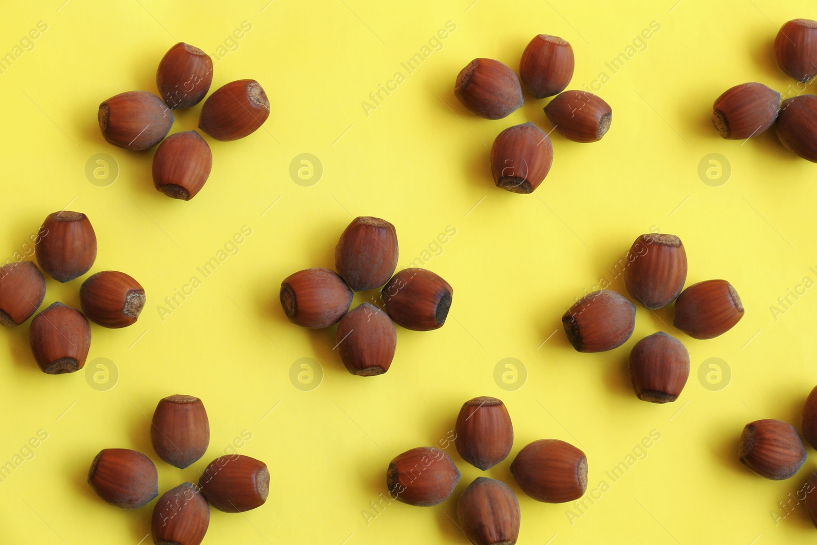 Photo of Pattern of hazelnuts on yellow background, flat lay