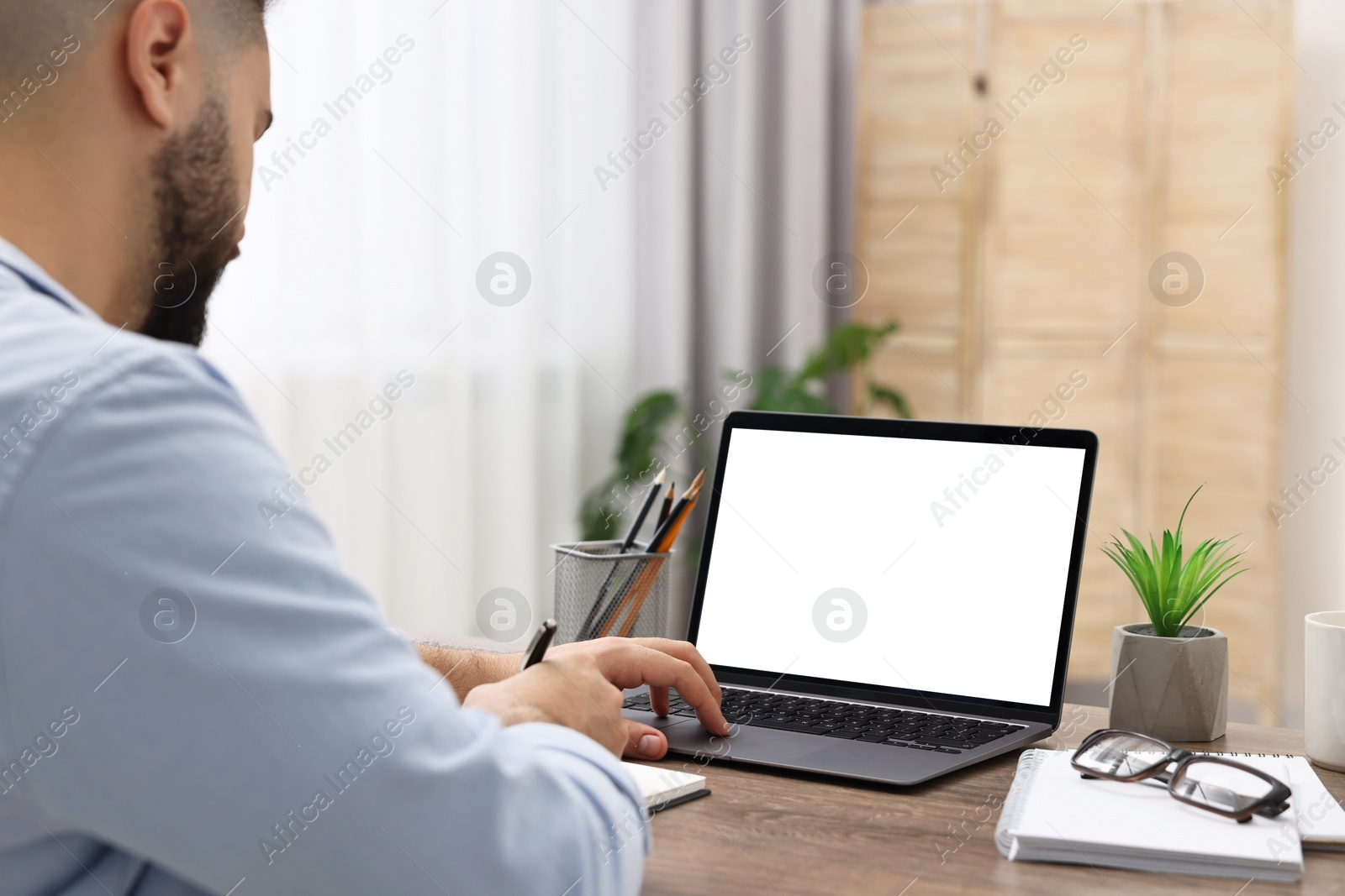 Photo of E-learning. Young man using laptop at wooden table indoors, closeup