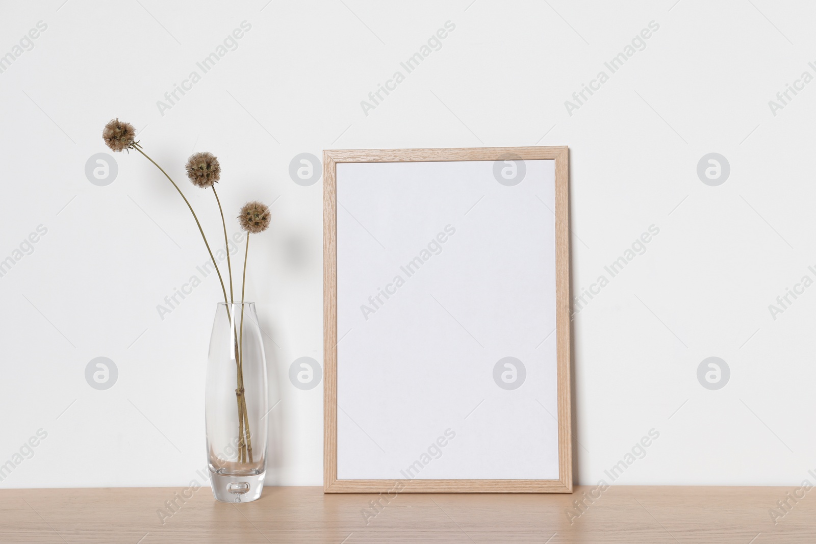 Photo of Empty photo frame and vase with dry decorative flowers on wooden table. Mockup for design