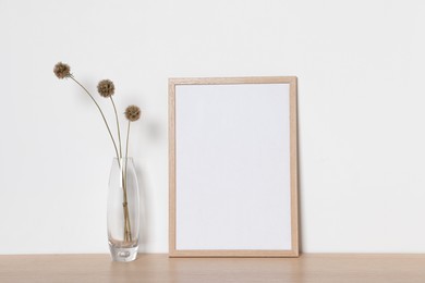 Photo of Empty photo frame and vase with dry decorative flowers on wooden table. Mockup for design