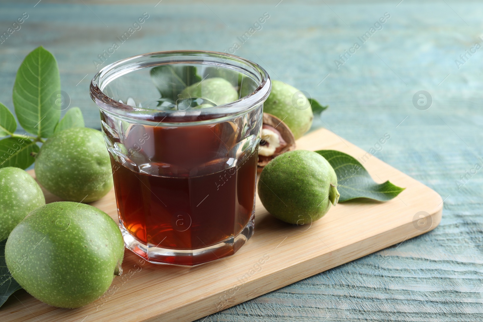 Photo of Delicious liqueur and green walnuts on light blue wooden table, closeup