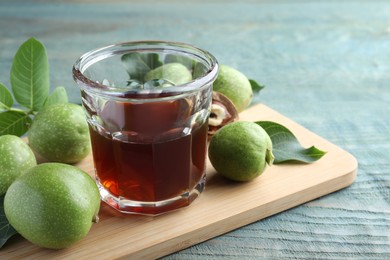 Photo of Delicious liqueur and green walnuts on light blue wooden table, closeup