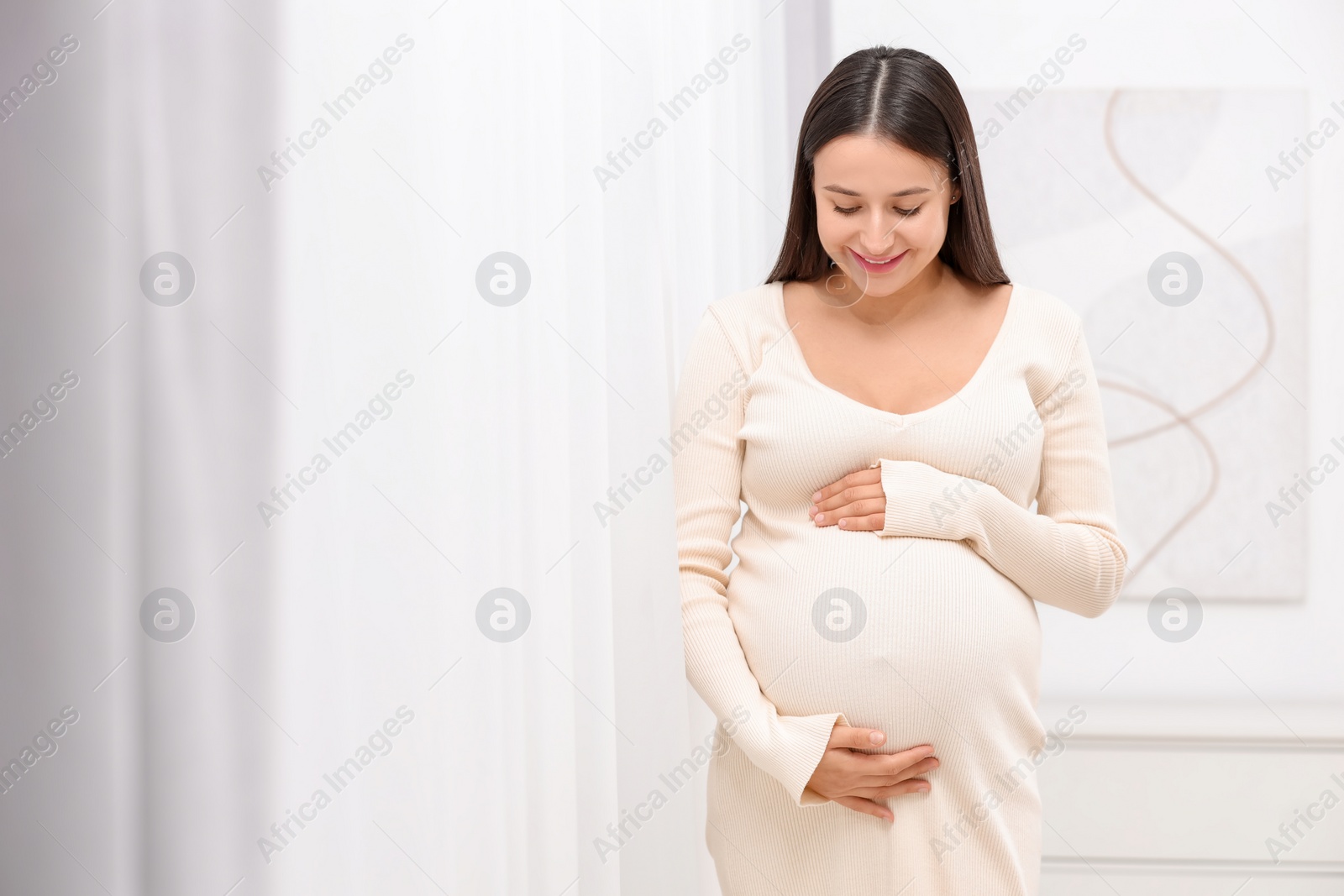 Photo of Beautiful pregnant woman in white dress indoors, space for text
