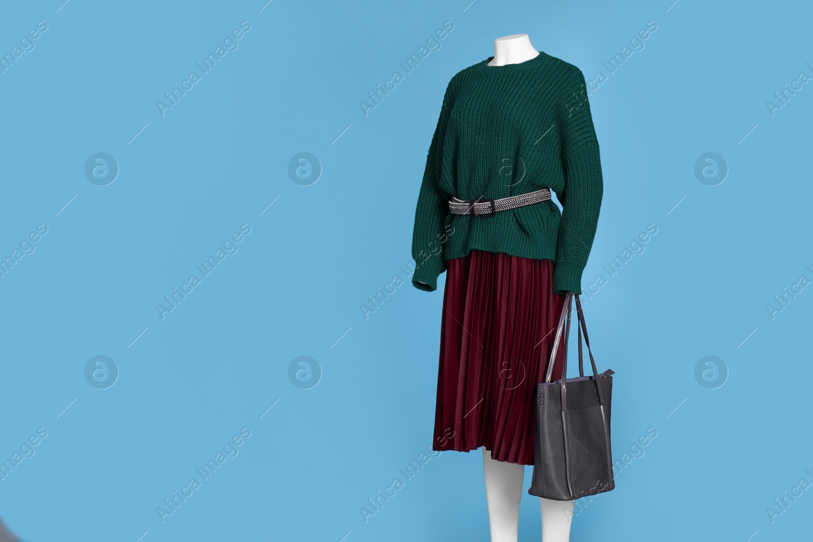 Photo of Female mannequin with bag dressed in dark green sweater with belt and skirt on light blue background, space for text