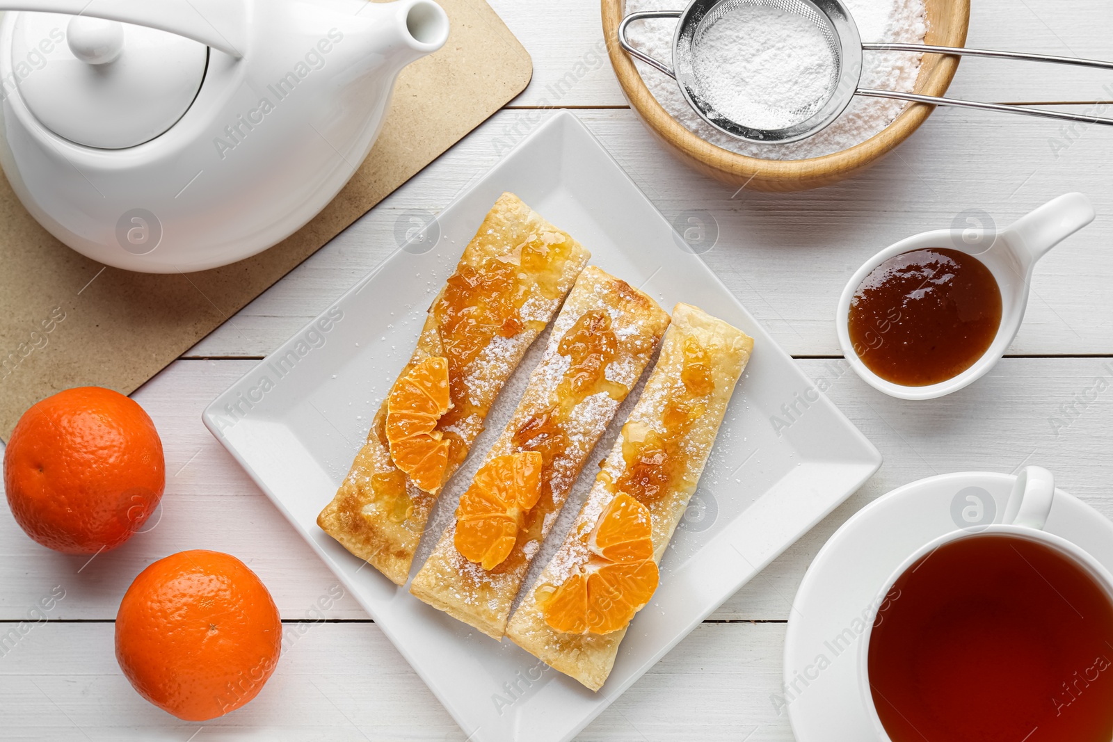 Photo of Fresh tasty puff pastry with sugar powder, jam and tangerines served on white wooden table, flat lay