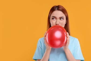 Photo of Woman inflating red balloon on orange background, space for text