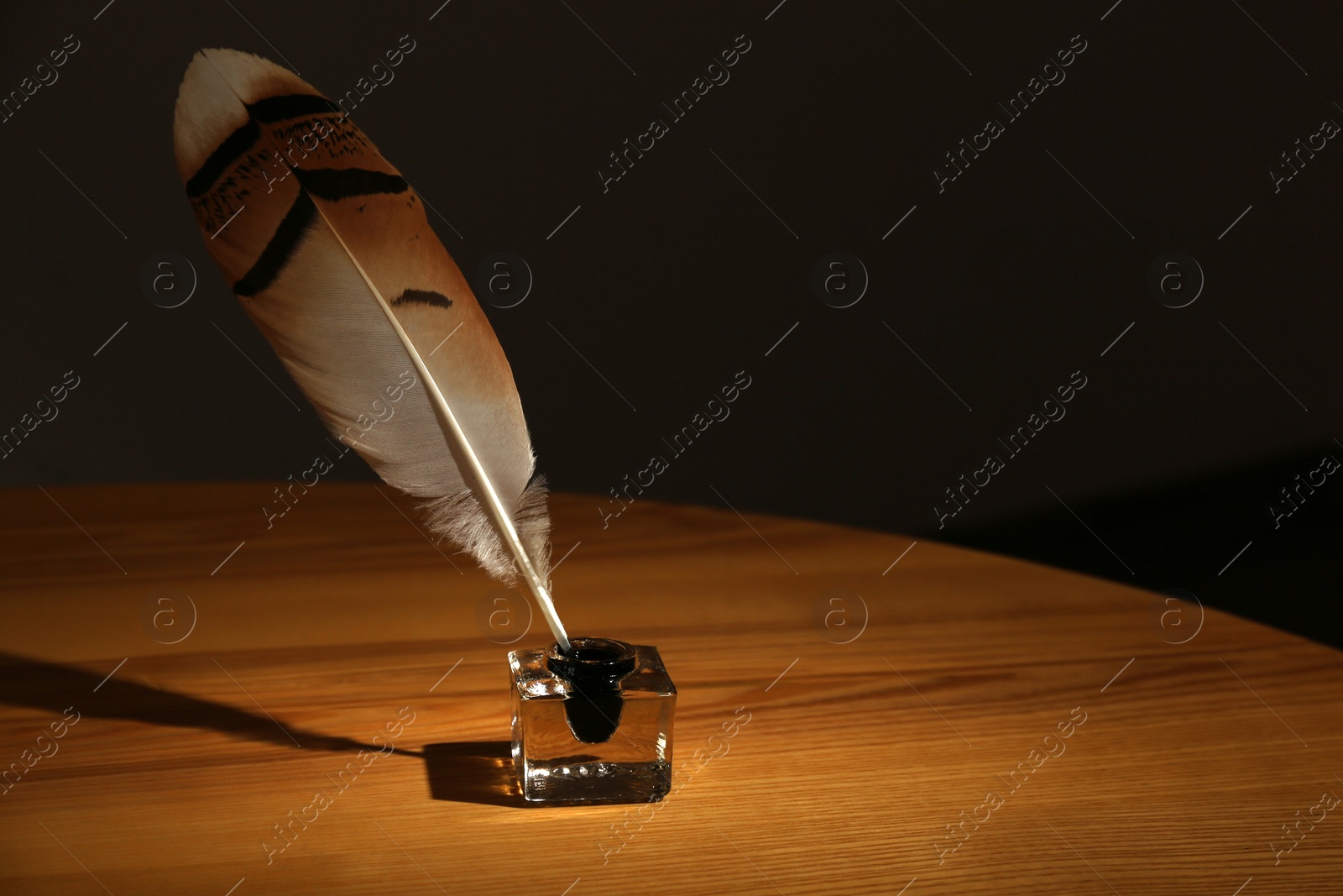 Photo of Feather pen and inkwell on wooden table in darkness. Space for text