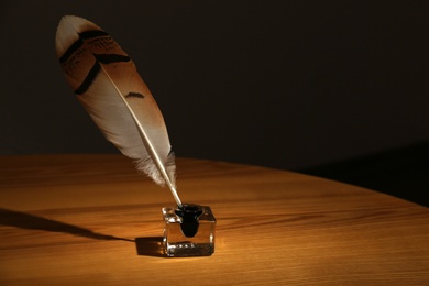 Photo of Feather pen and inkwell on wooden table in darkness. Space for text