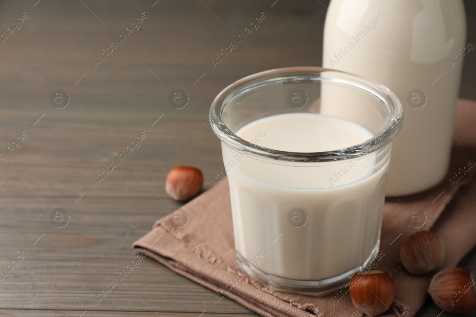 Photo of Glassware with lactose free milk and hazelnuts on wooden table, closeup. Space for text