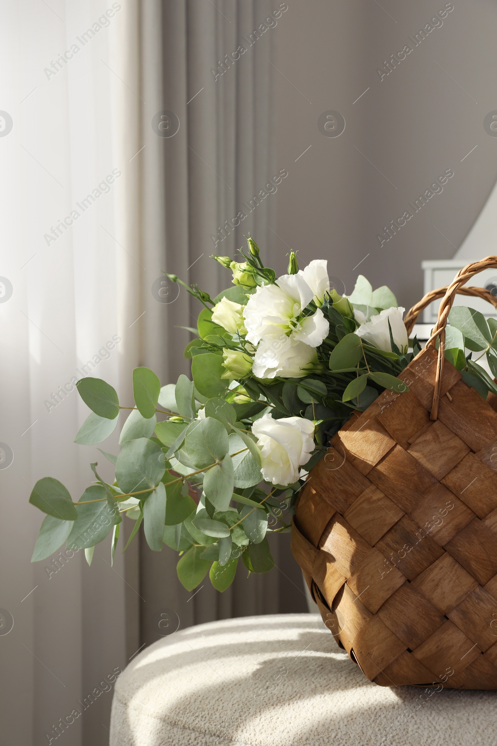 Photo of Stylish wicker basket with bouquet of flowers on ottoman in room