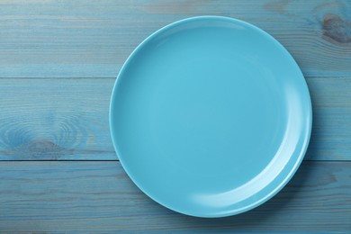 Empty ceramic plate on light blue wooden table, top view. Space for text