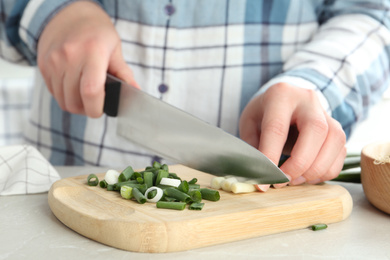 Woman cutting green spring onions on wooden board at table, closeup