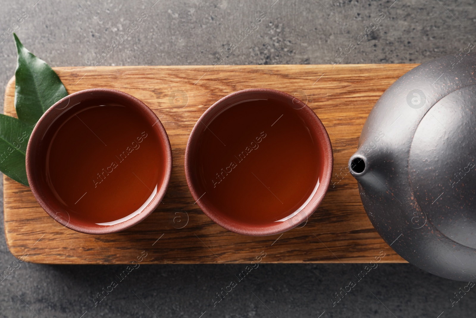 Photo of Board with cups and teapot of freshly brewed oolong on grey background, top view