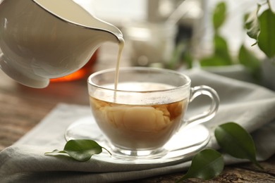 Photo of Pouring milk into cup with tea on wooden table, closeup
