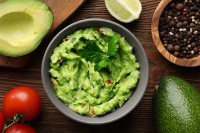 Photo of Delicious guacamole and ingredients on wooden table, flat lay