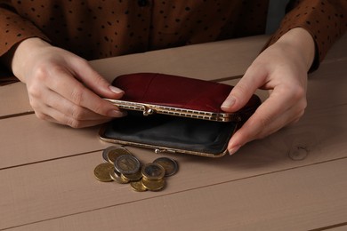 Photo of Poverty. Woman with empty wallet and coins at wooden table, closeup
