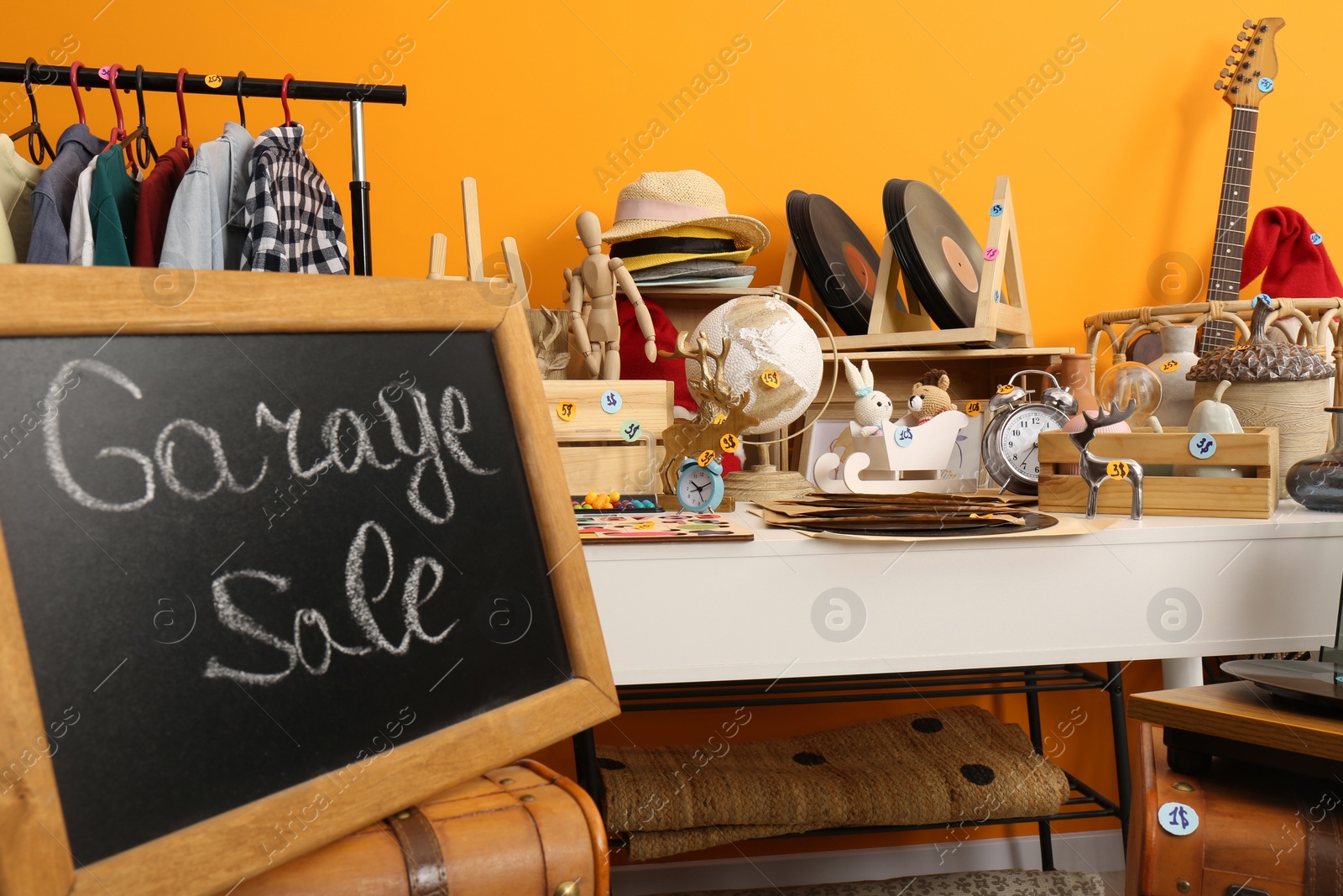 Photo of Sign Garage Sale written on blackboard near many different stuff indoors