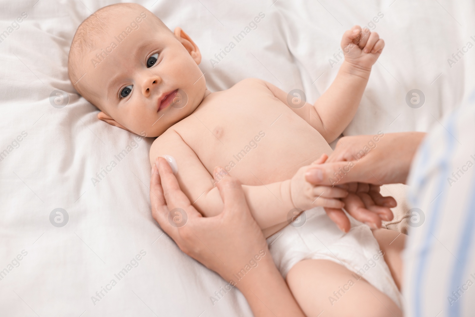 Photo of Woman applying body cream onto baby`s skin on bed, above view